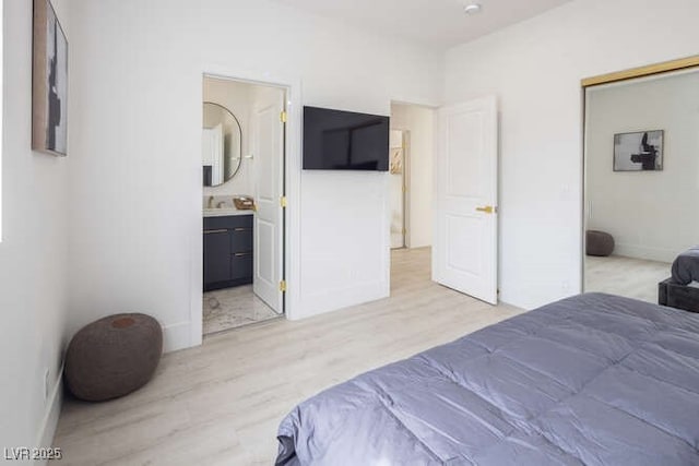 bedroom with light wood-style floors, baseboards, and ensuite bathroom