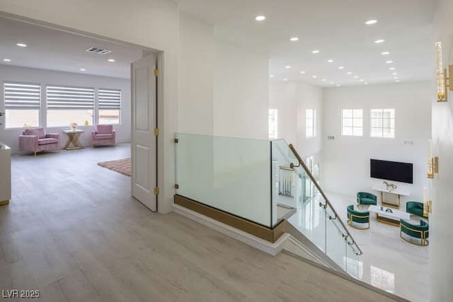 corridor with visible vents, a wealth of natural light, wood finished floors, and an upstairs landing