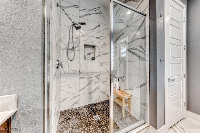 bathroom with a textured wall, a marble finish shower, and vanity