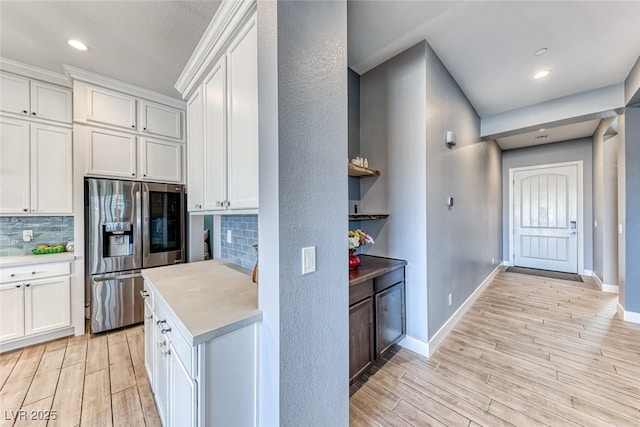 kitchen with light wood finished floors, light countertops, decorative backsplash, white cabinets, and stainless steel fridge