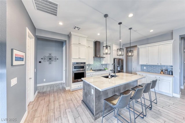 kitchen featuring stainless steel appliances, visible vents, a sink, and wall chimney range hood