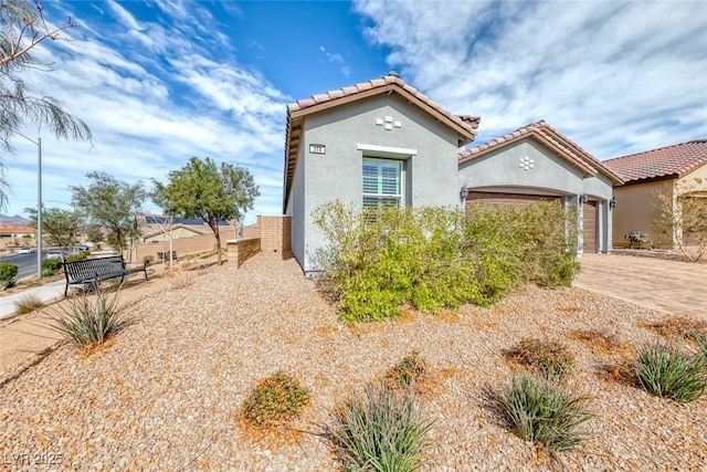 view of front facade featuring a garage, a tile roof, fence, decorative driveway, and stucco siding