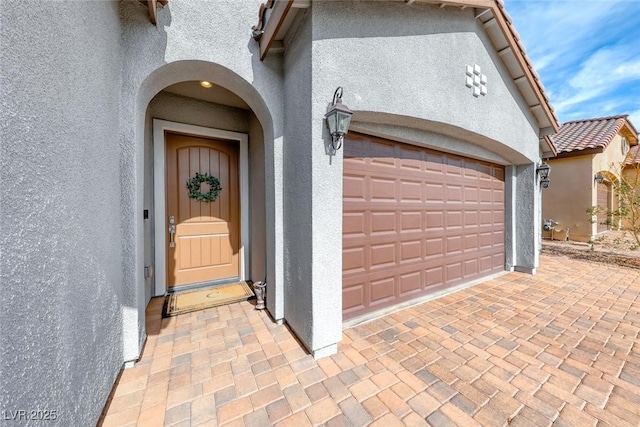 view of exterior entry featuring a garage, decorative driveway, a tile roof, and stucco siding