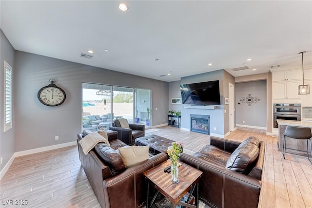 living area featuring light wood-type flooring, recessed lighting, visible vents, and a glass covered fireplace