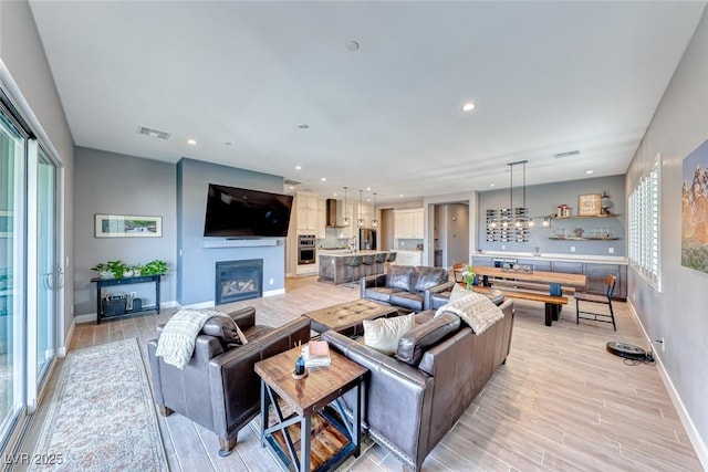 living area featuring a healthy amount of sunlight, light wood-style flooring, visible vents, and a glass covered fireplace