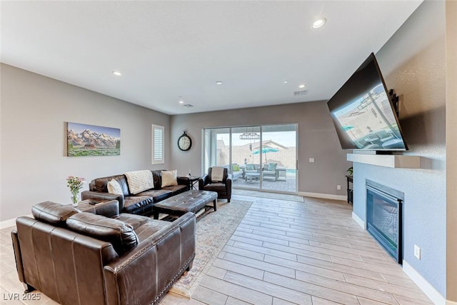 living room with wood finish floors, recessed lighting, visible vents, a glass covered fireplace, and baseboards