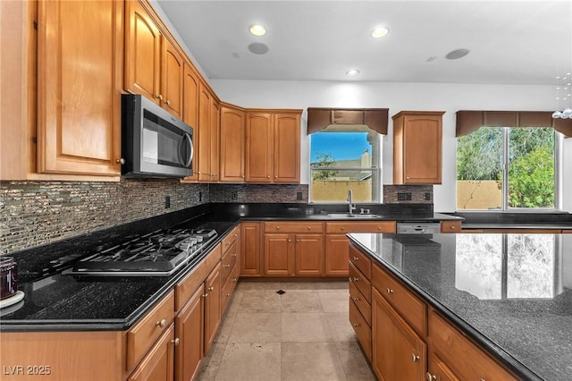 kitchen featuring tasteful backsplash, stainless steel microwave, dark stone counters, gas cooktop, and a sink