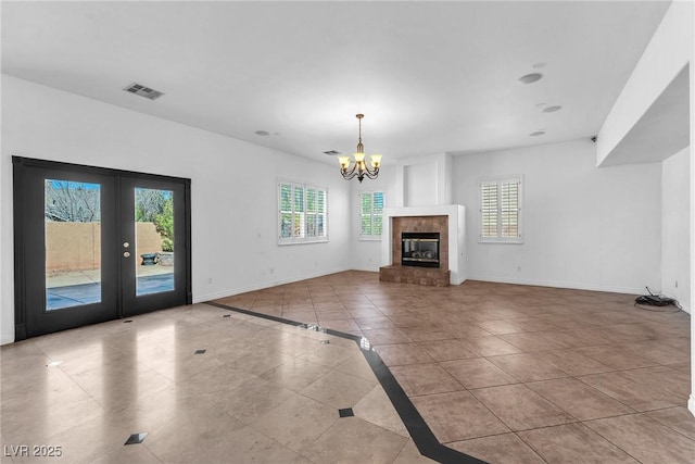 unfurnished living room with visible vents, baseboards, a chandelier, french doors, and a glass covered fireplace