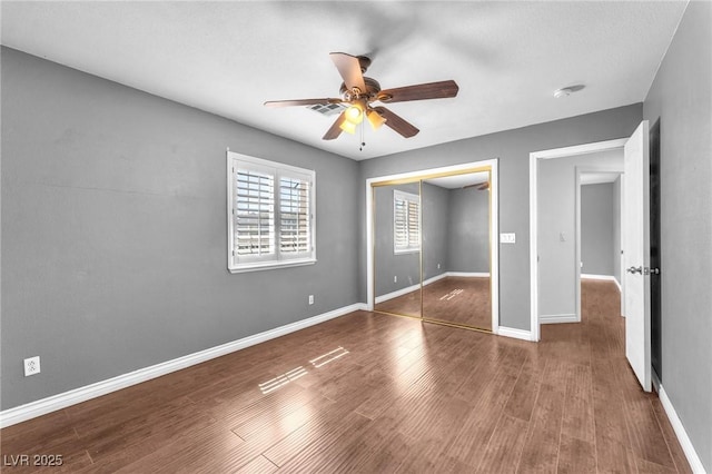 unfurnished bedroom with wood finished floors, visible vents, baseboards, ceiling fan, and a closet