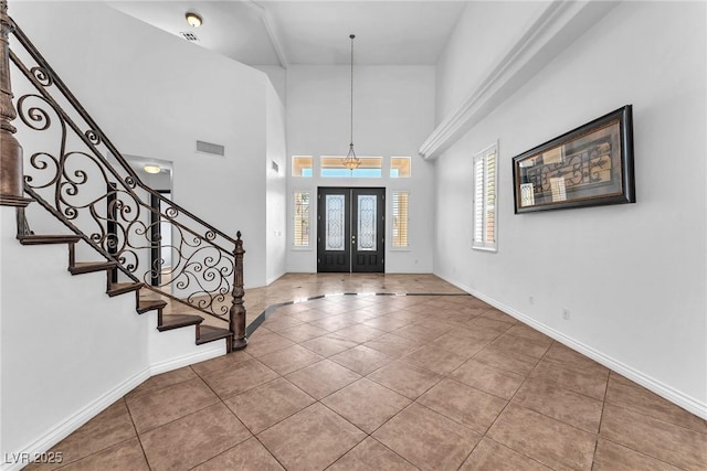 tiled foyer entrance featuring french doors, baseboards, a towering ceiling, and stairs