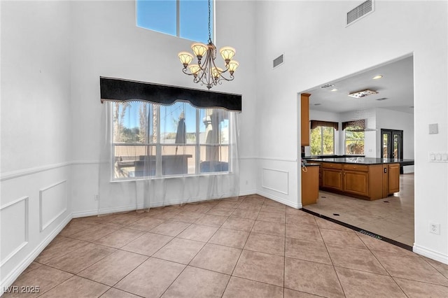 unfurnished dining area with a decorative wall, a notable chandelier, visible vents, and light tile patterned floors