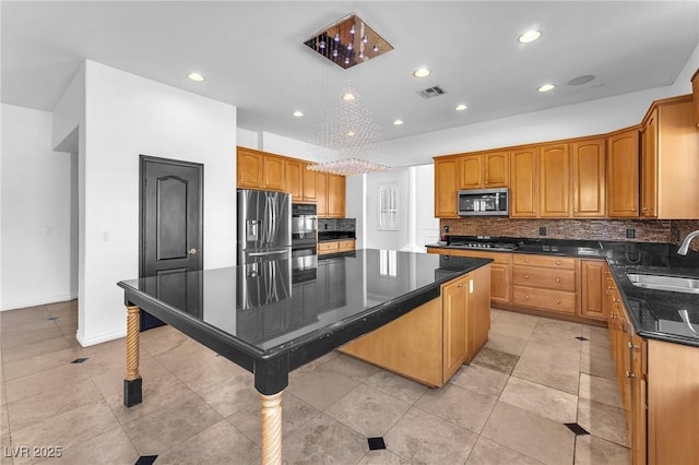 kitchen featuring visible vents, backsplash, a kitchen island, stainless steel appliances, and a sink