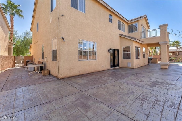 back of property featuring stucco siding, a patio, a balcony, and fence