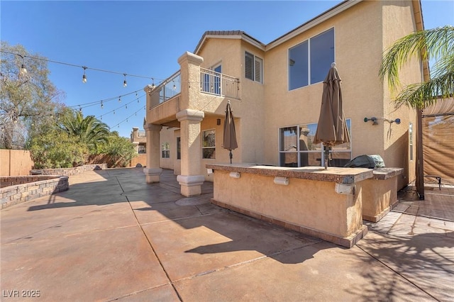 exterior space featuring stucco siding, a balcony, a patio area, and an outdoor kitchen