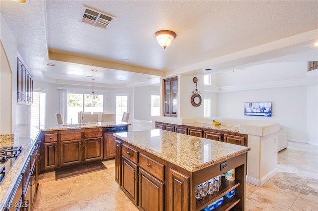 kitchen with light stone counters, visible vents, a peninsula, brown cabinets, and a center island