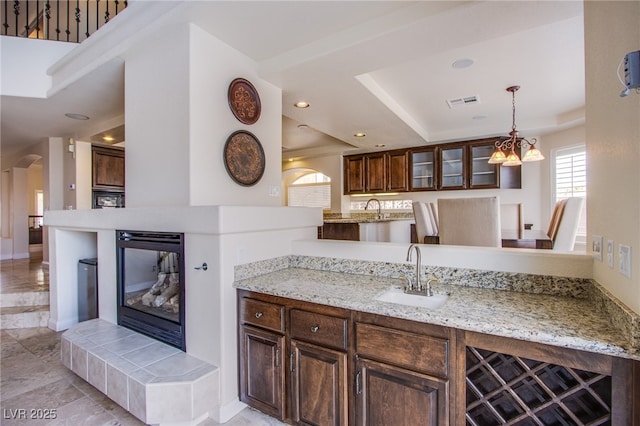 kitchen featuring recessed lighting, arched walkways, a sink, glass insert cabinets, and a raised ceiling