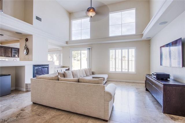 living room featuring visible vents, a high ceiling, baseboards, and a glass covered fireplace