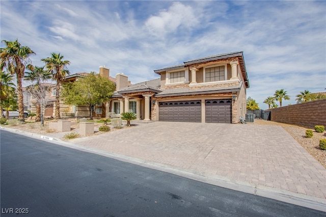 view of front facade with fence, a chimney, stucco siding, a garage, and decorative driveway