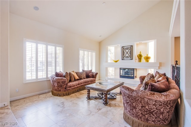 living area featuring a glass covered fireplace, high vaulted ceiling, and baseboards