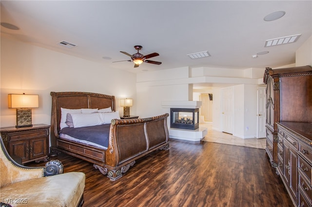 bedroom featuring visible vents, a multi sided fireplace, and wood finished floors