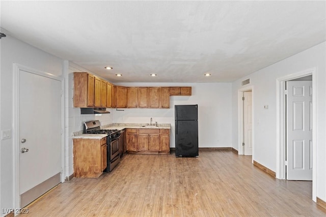 kitchen featuring stainless steel gas stove, visible vents, freestanding refrigerator, light countertops, and a sink