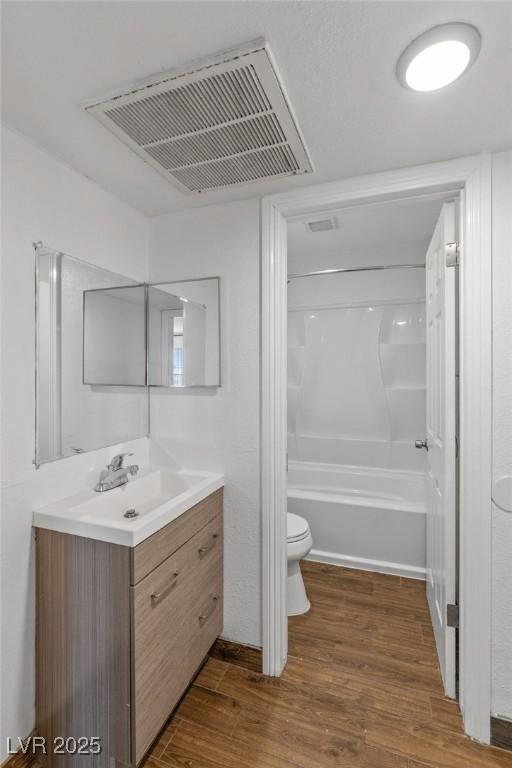 bathroom featuring toilet, wood finished floors, vanity, visible vents, and  shower combination