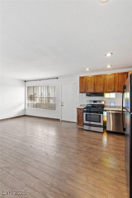 kitchen with brown cabinets, wood finished floors, open floor plan, light countertops, and stainless steel appliances