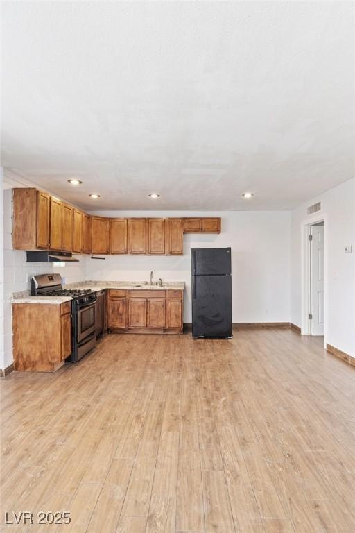 kitchen with stainless steel range with gas cooktop, brown cabinets, light wood finished floors, visible vents, and freestanding refrigerator