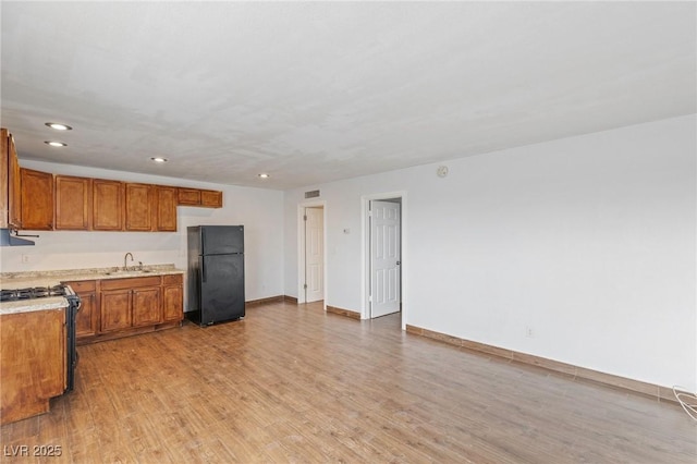 kitchen featuring brown cabinets, freestanding refrigerator, light countertops, light wood-style floors, and gas stove