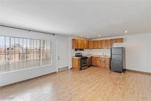 kitchen featuring light wood finished floors, brown cabinets, freestanding refrigerator, light countertops, and gas stove