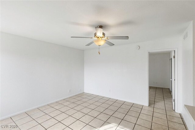 empty room featuring light tile patterned floors, a ceiling fan, and baseboards