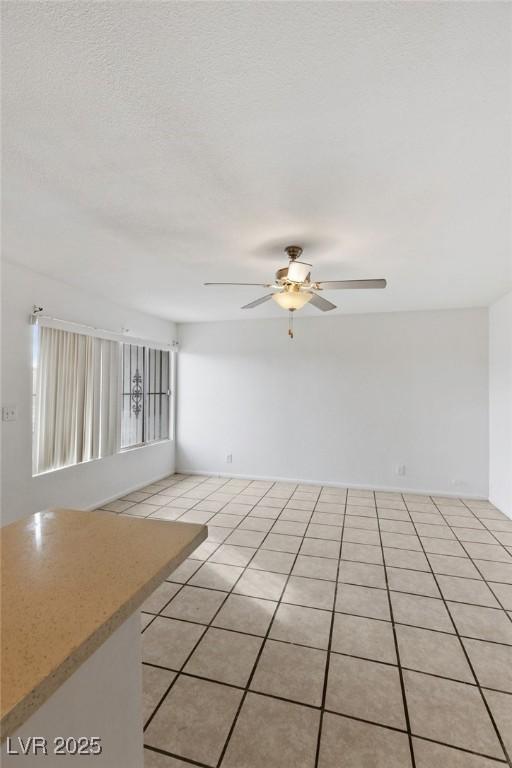 empty room with ceiling fan, a textured ceiling, and light tile patterned floors