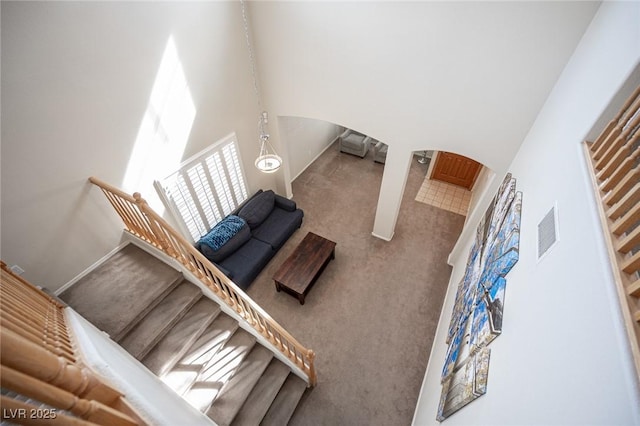 living room with arched walkways, carpet, visible vents, stairway, and a towering ceiling