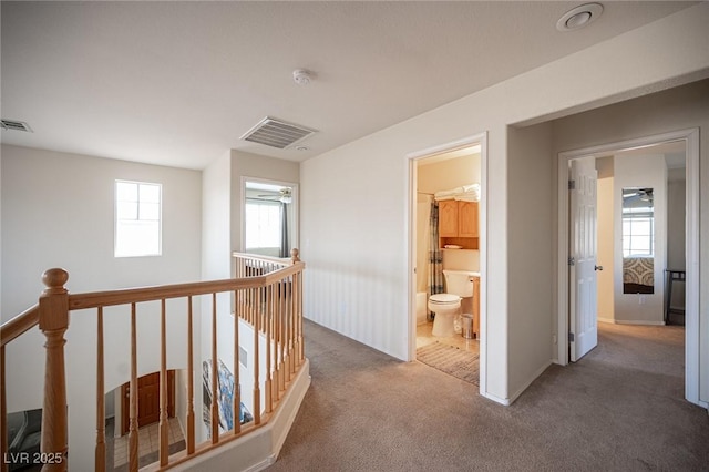 hallway with carpet floors, visible vents, and an upstairs landing