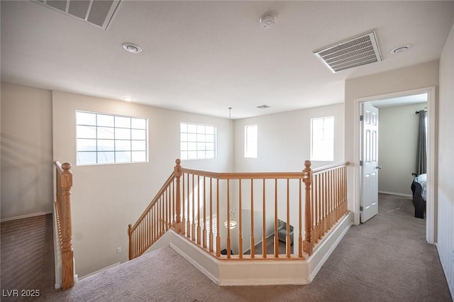 corridor featuring carpet, visible vents, baseboards, and an upstairs landing