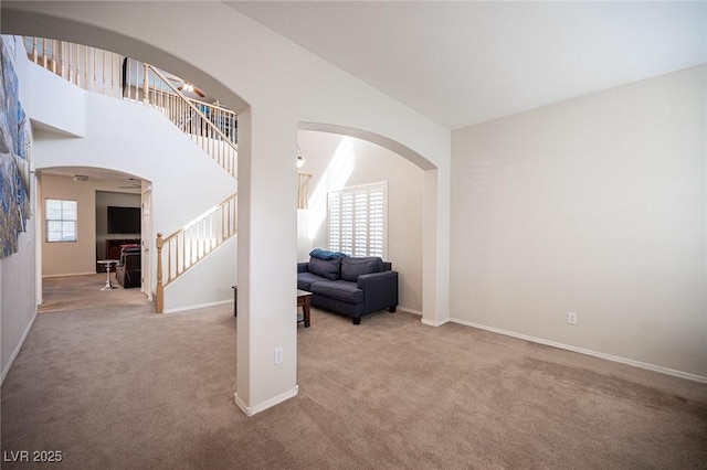 interior space with baseboards, arched walkways, a towering ceiling, carpet, and stairs