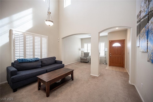 carpeted living area with baseboards, a high ceiling, and arched walkways