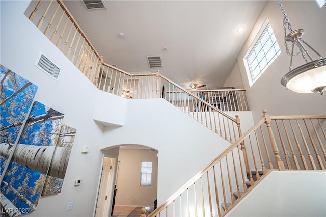 staircase with a high ceiling, visible vents, and arched walkways