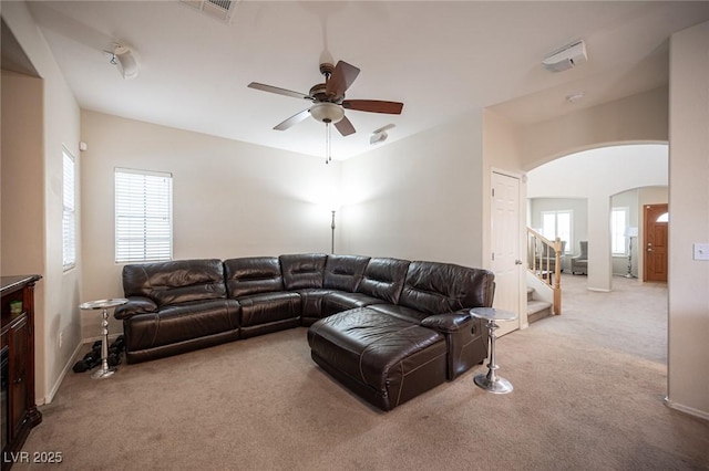 carpeted living room with a ceiling fan, arched walkways, a healthy amount of sunlight, and stairs