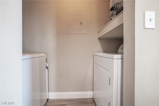 clothes washing area featuring wood finished floors, laundry area, electric panel, independent washer and dryer, and baseboards