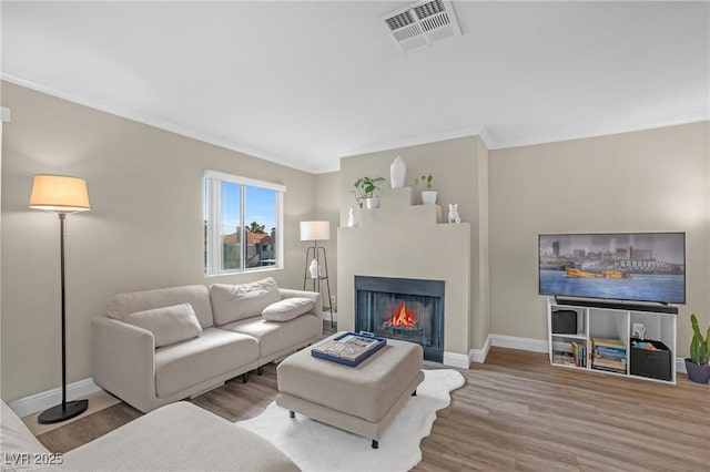 living room featuring wood finished floors, visible vents, baseboards, a lit fireplace, and crown molding