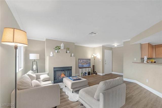 living area with a warm lit fireplace, baseboards, visible vents, crown molding, and light wood-style floors