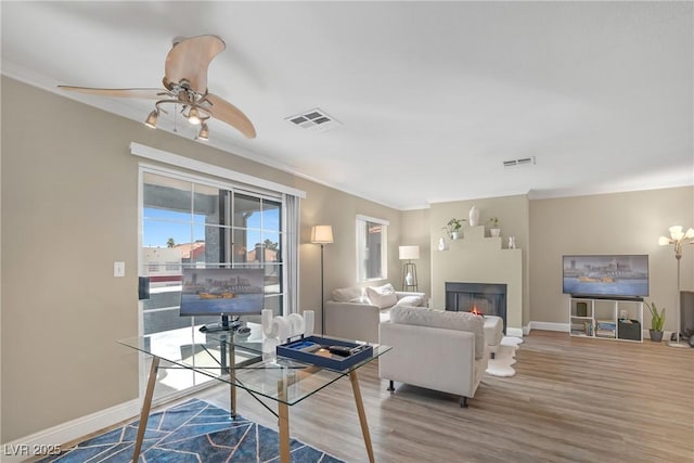 living room featuring baseboards, a lit fireplace, visible vents, and wood finished floors