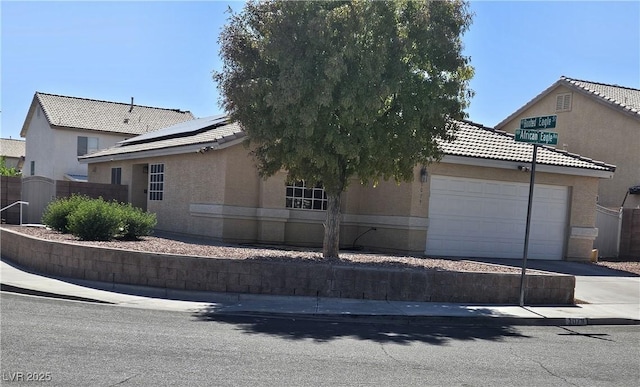 view of front of property with an attached garage, fence, driveway, roof mounted solar panels, and stucco siding