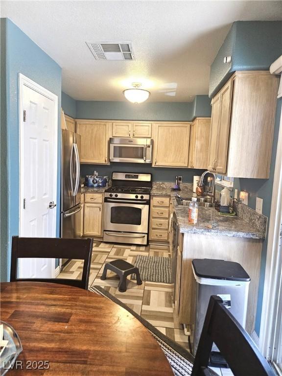 kitchen featuring light wood finished floors, visible vents, appliances with stainless steel finishes, light brown cabinets, and a sink