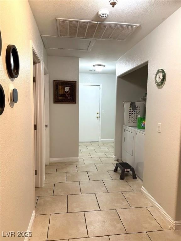 corridor with light tile patterned floors, baseboards, visible vents, a textured ceiling, and washer and dryer