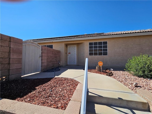 property entrance with a tile roof, a gate, fence, and stucco siding