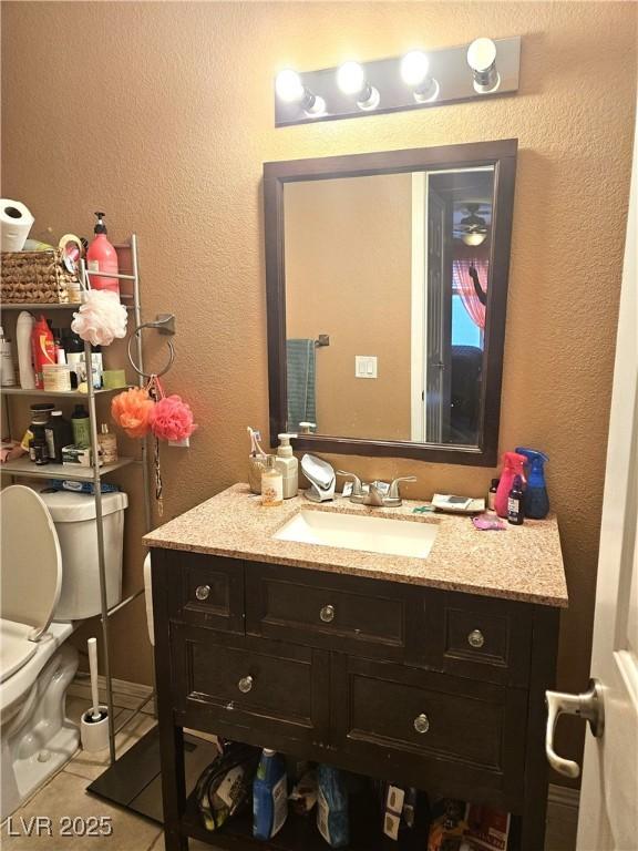 half bath with toilet, a textured wall, vanity, and tile patterned floors