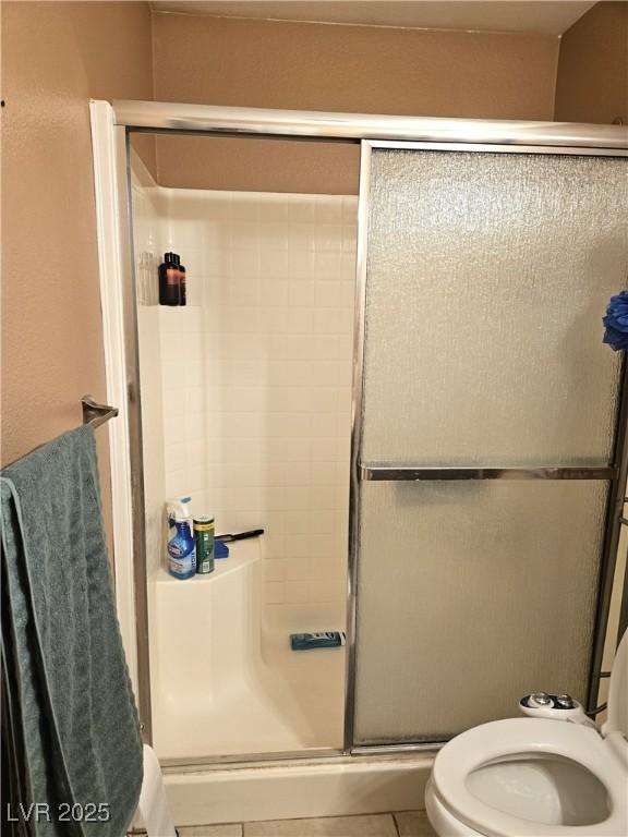 bathroom featuring toilet, a stall shower, and tile patterned flooring