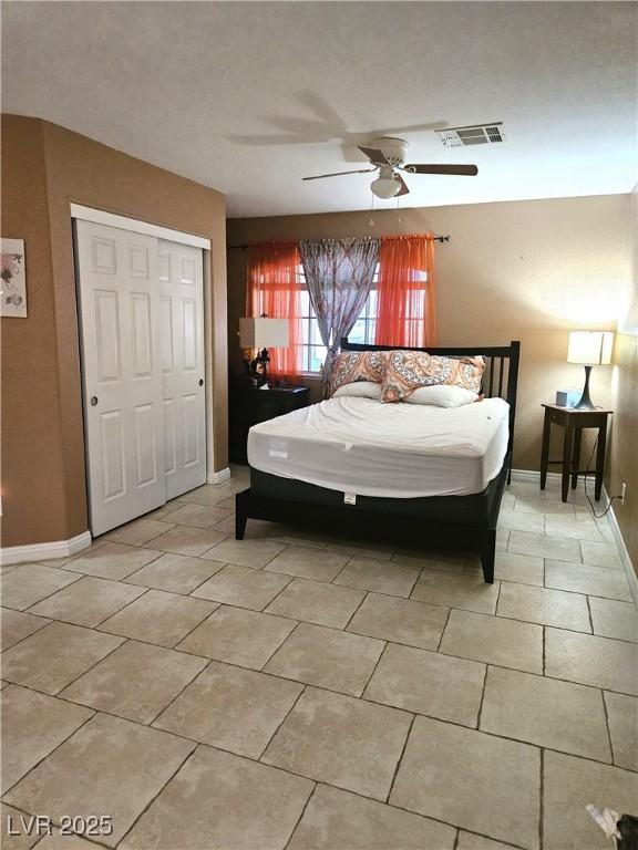 bedroom featuring a ceiling fan, a closet, light tile patterned flooring, and baseboards